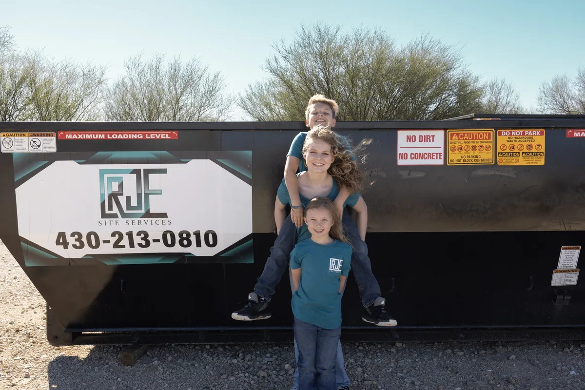 The Eggering kids in RJE Site Services shirts in front of an RJE roll-off dumpster